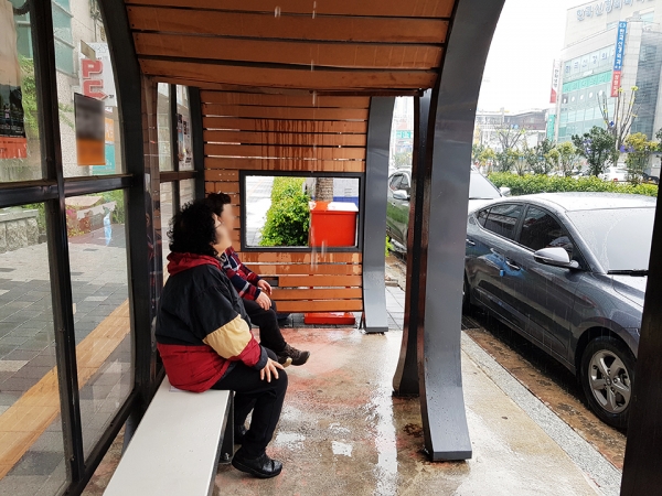 버스승강장 지붕에서 떨어지는 빗물을 바라보고 있는 주민.