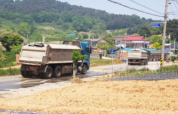 덤프트럭 2대가 줄지어 마을 앞을 지나가고 있다.